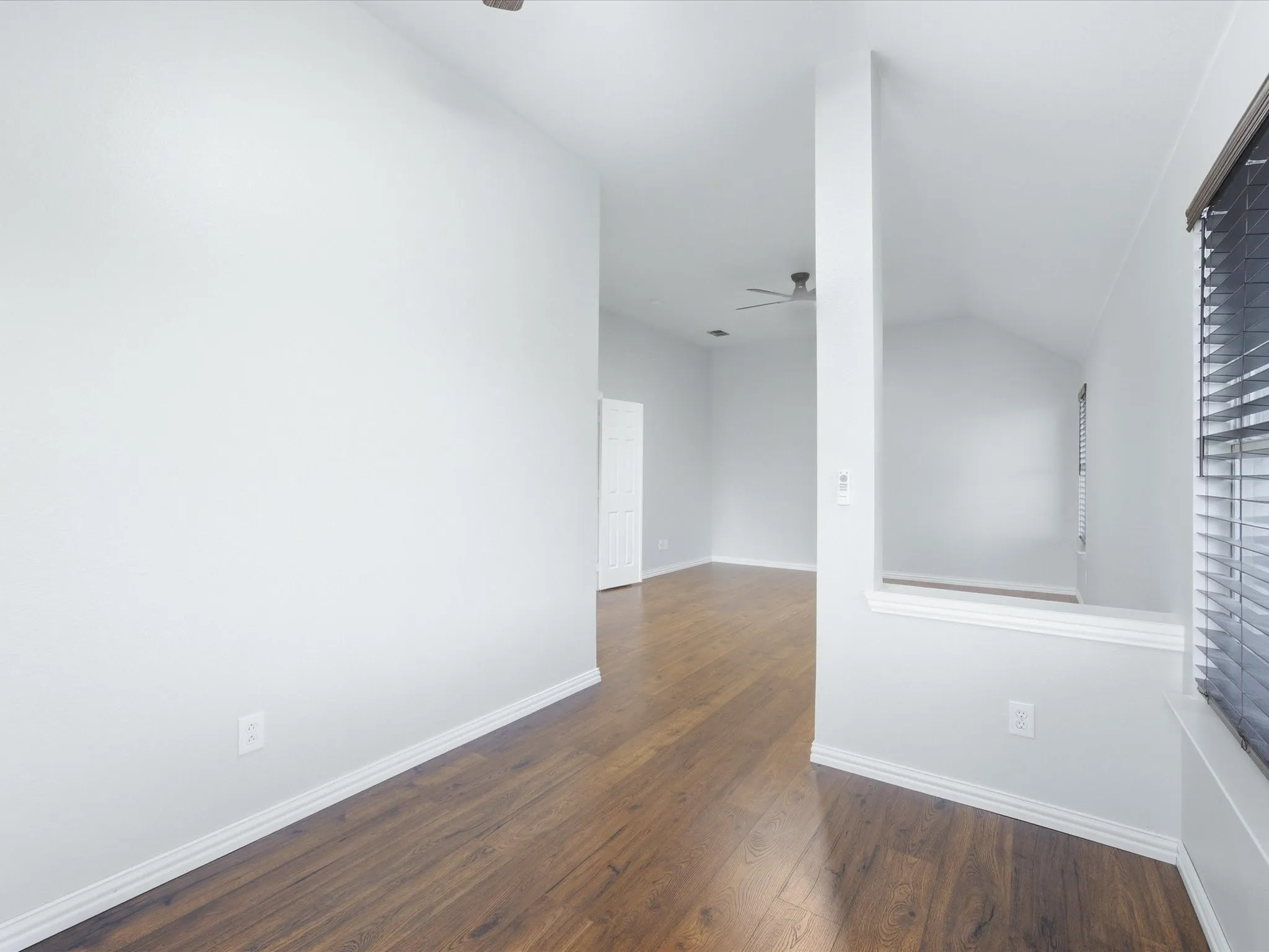 Wood-finish flooring, white walls, ceiling fan, window with blinds, and white trim