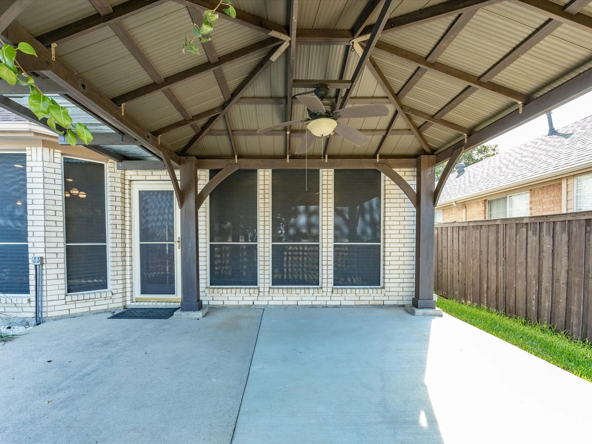 Covered patio with a corrugated metal roof, wood-finish support beams, and an integrated ceiling fan