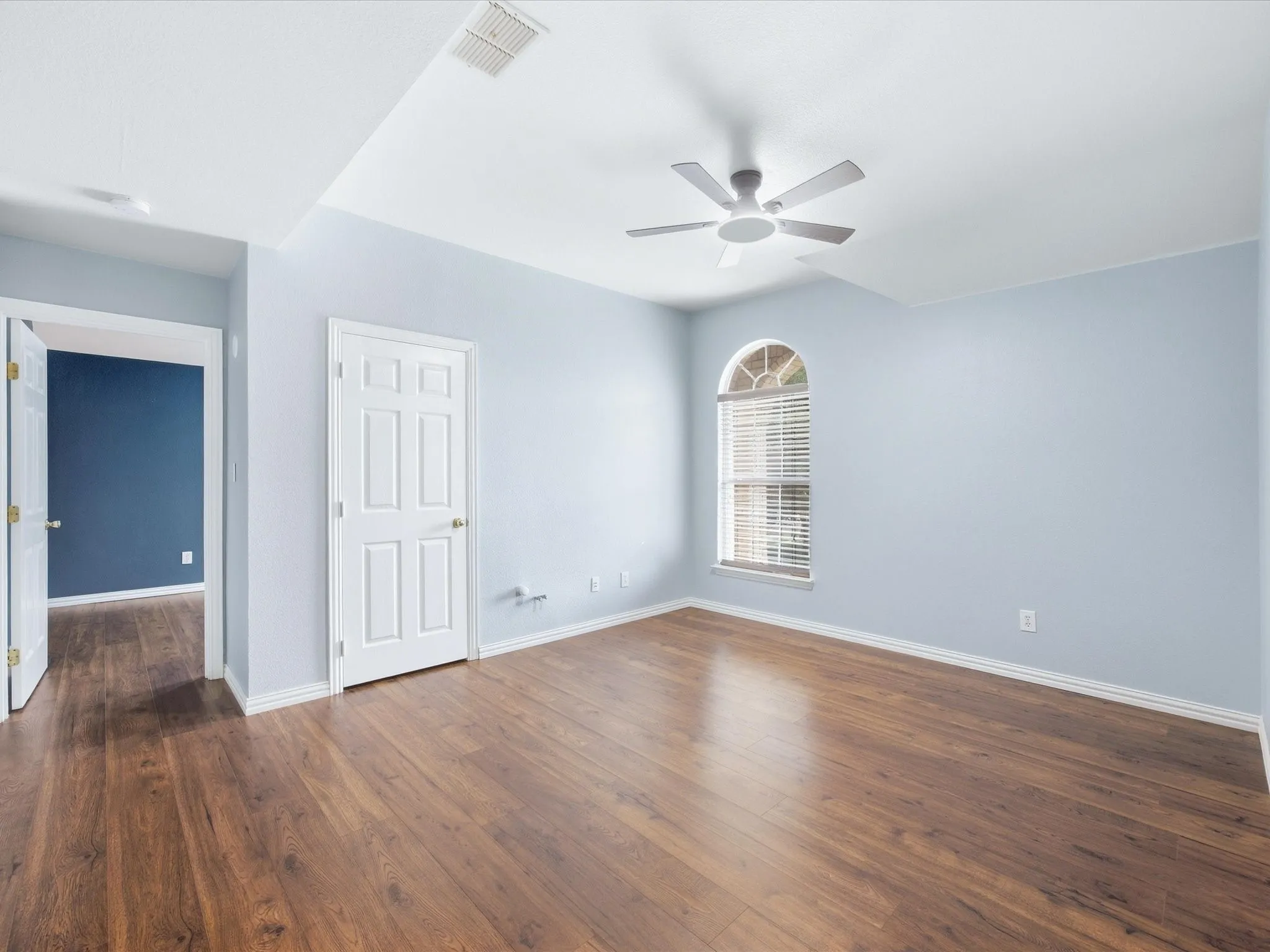 Wood-finish flooring, vaulted ceiling, and an arched window with blinds