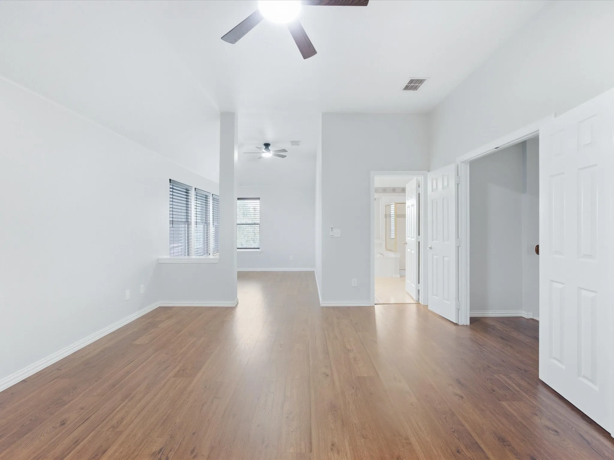 Vaulted ceiling, wood-finish flooring, ceiling fan with integrated lighting, multiple windows with blinds, and white interior paint