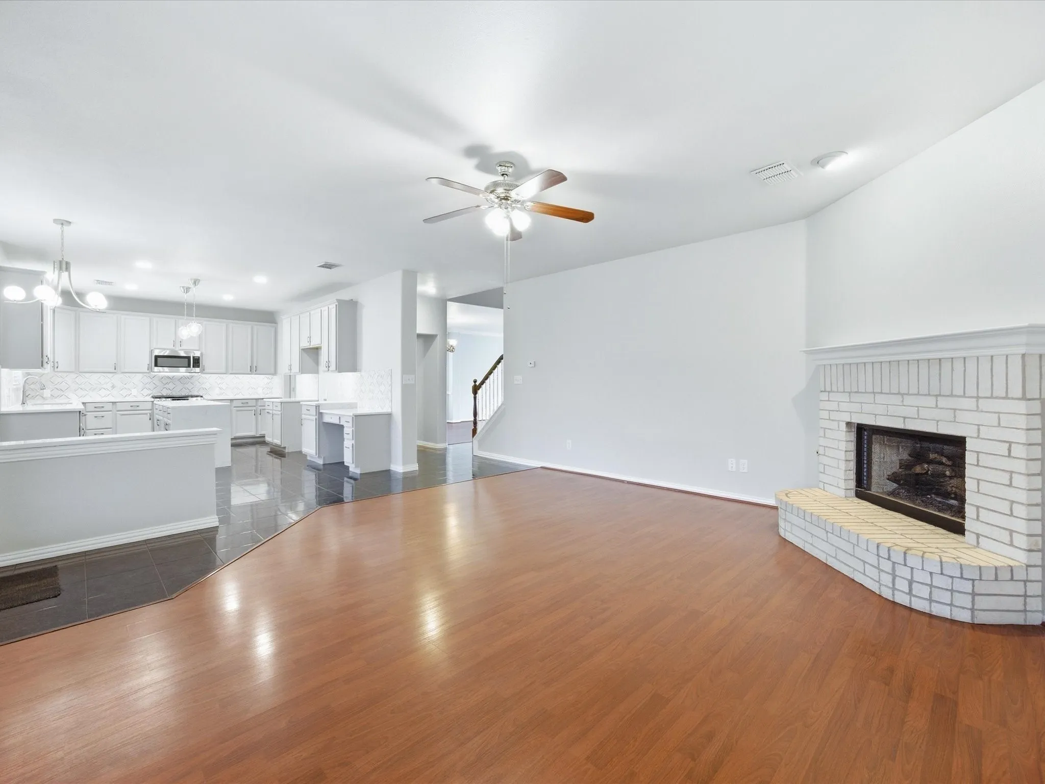 Hardwood-style flooring throughout, white brick fireplace, ceiling fan with light fixture, built-in cabinetry, and tile flooring