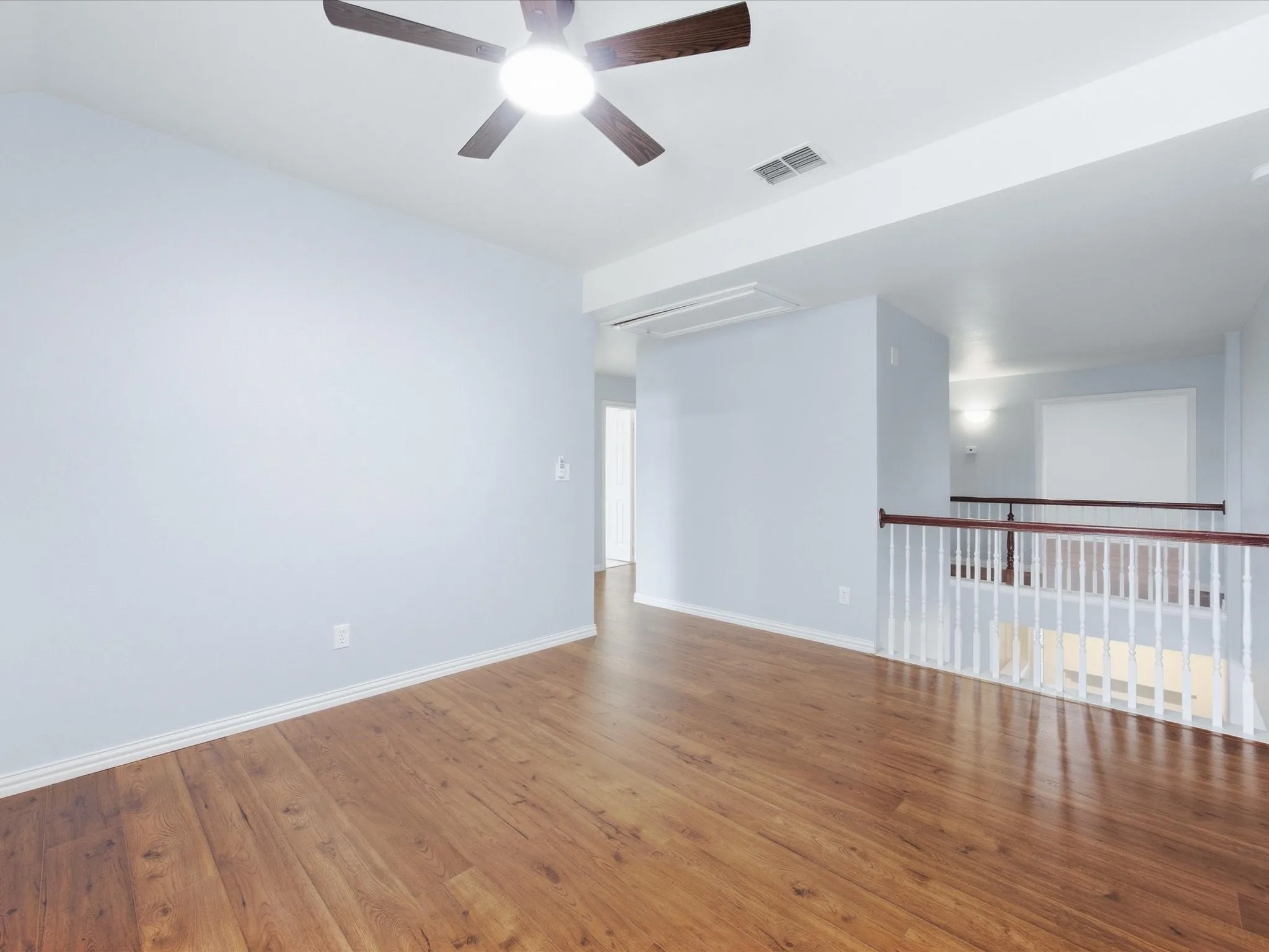 Wood-finish flooring, ceiling fan with integrated lighting, white wall paint, and white painted railing with wood-finish top