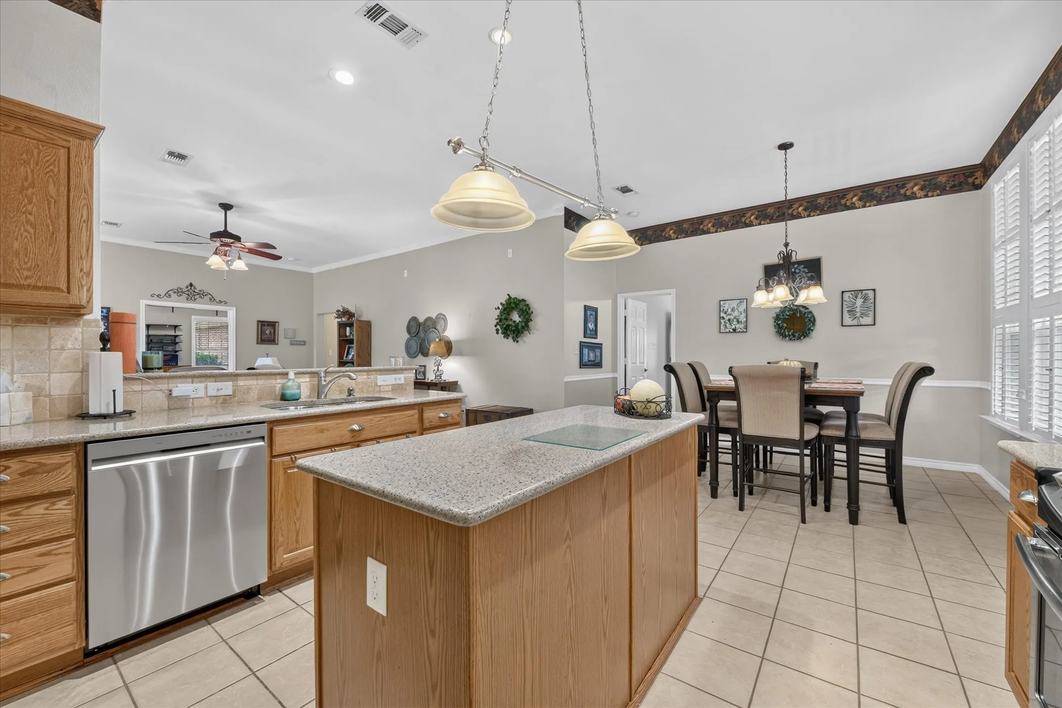 Kitchen featuring wood-finish cabinetry, stainless steel dishwasher, and a center island with a light-toned countertop