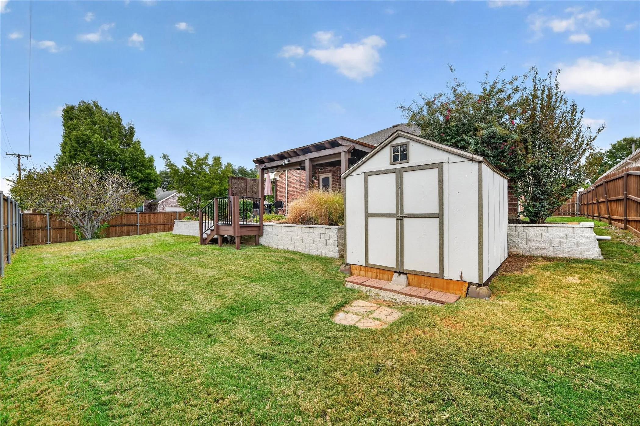 Expansive backyard featuring a storage shed, tiered retaining walls, a wood-plank deck, and perimeter wood fencing