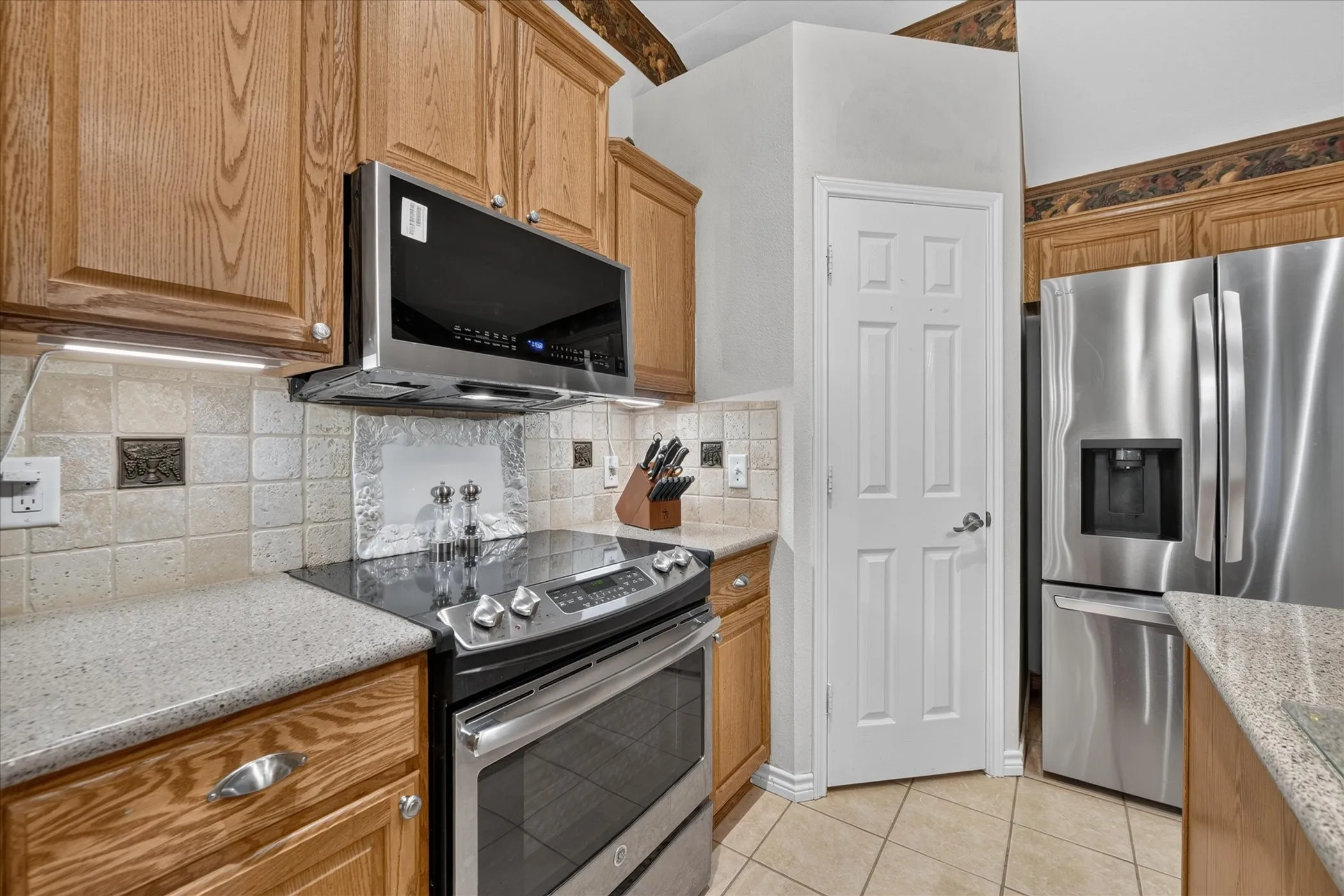 Oak wood cabinetry, stainless steel appliances, stone tile backsplash, textured countertops, and tile flooring