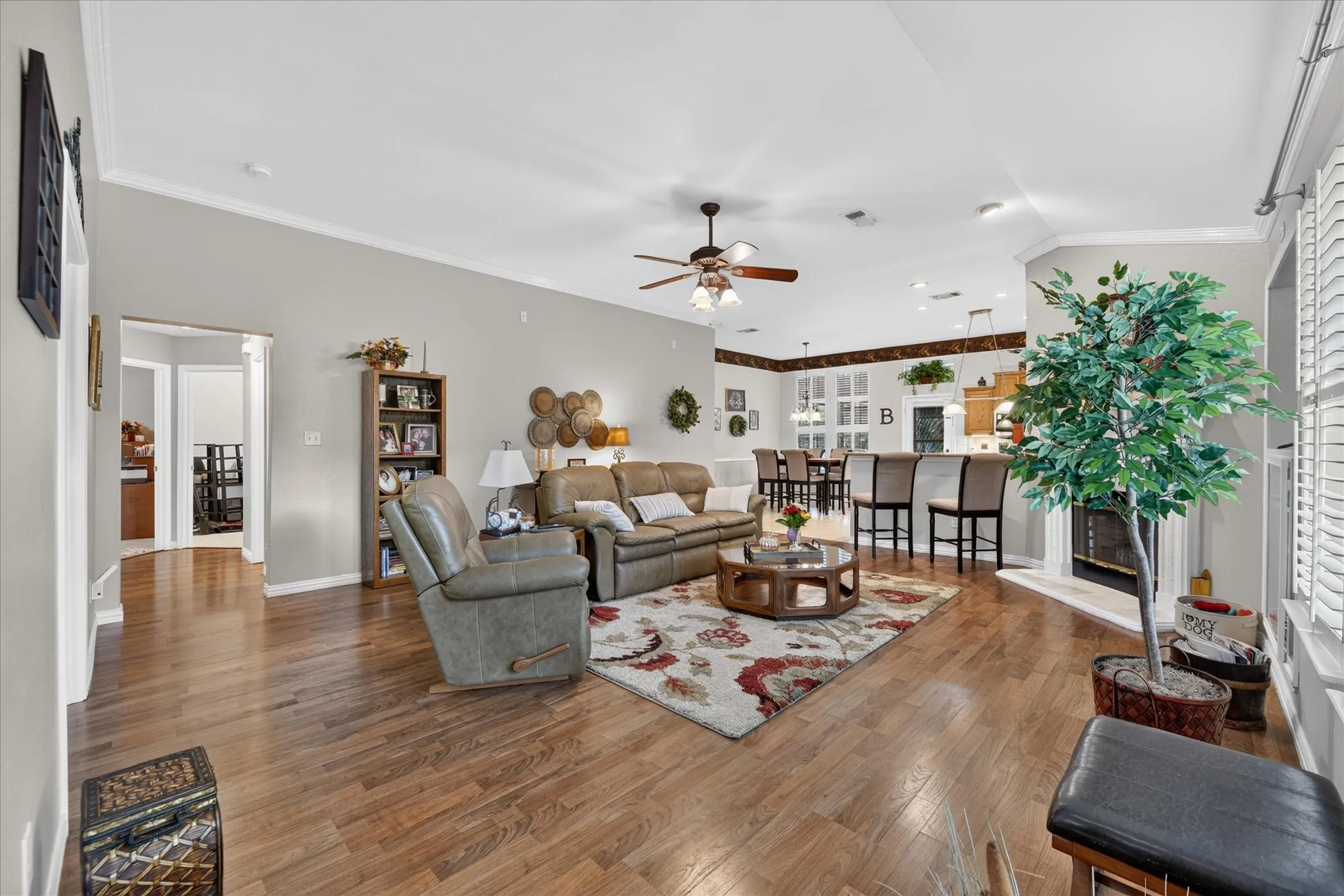 Hardwood-finish flooring, crown molding, white plantation-style shutters, ceiling fan, and a built-in fireplace