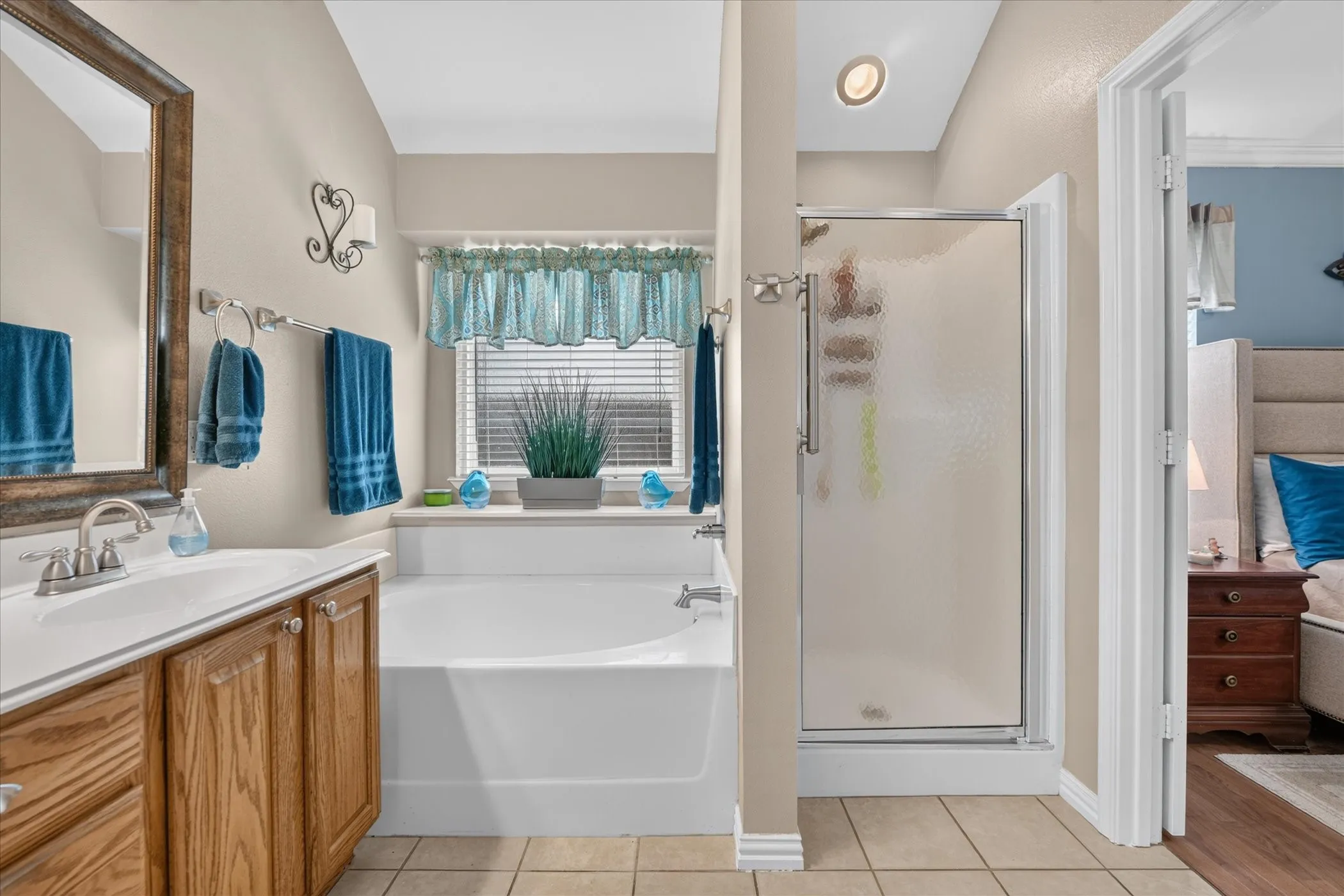 Built-in soaking tub, vanity with wood-finish cabinetry, chrome fixtures, and a glass-enclosed shower