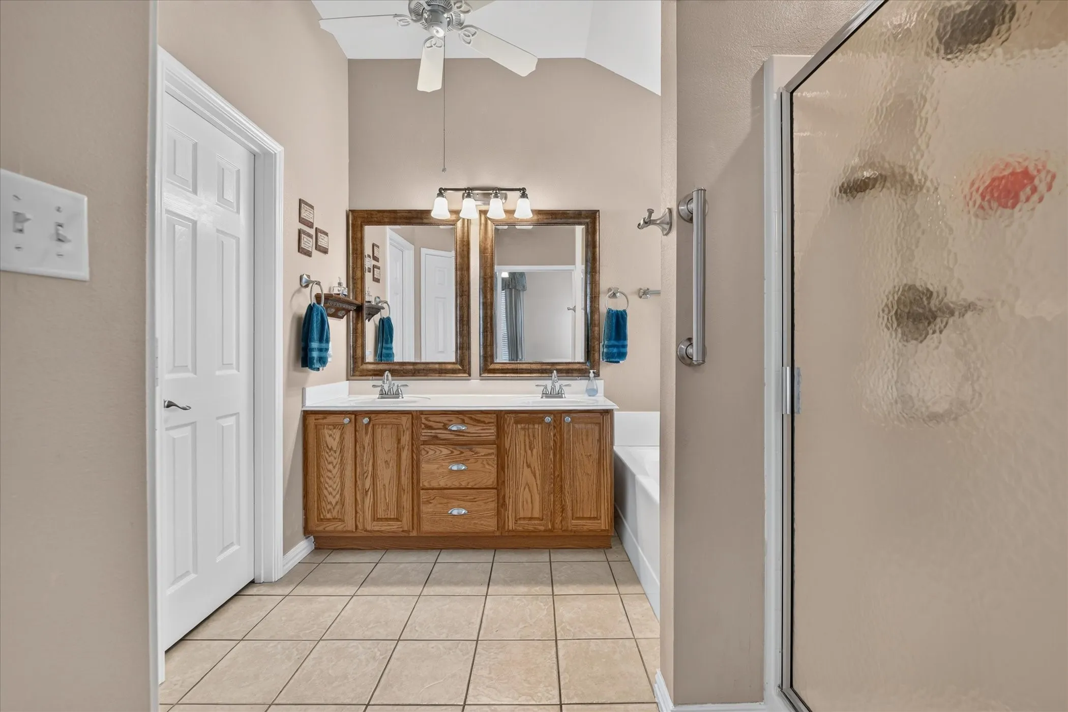 Dual vanity with wood-finish cabinetry, tile flooring, and a shower enclosure