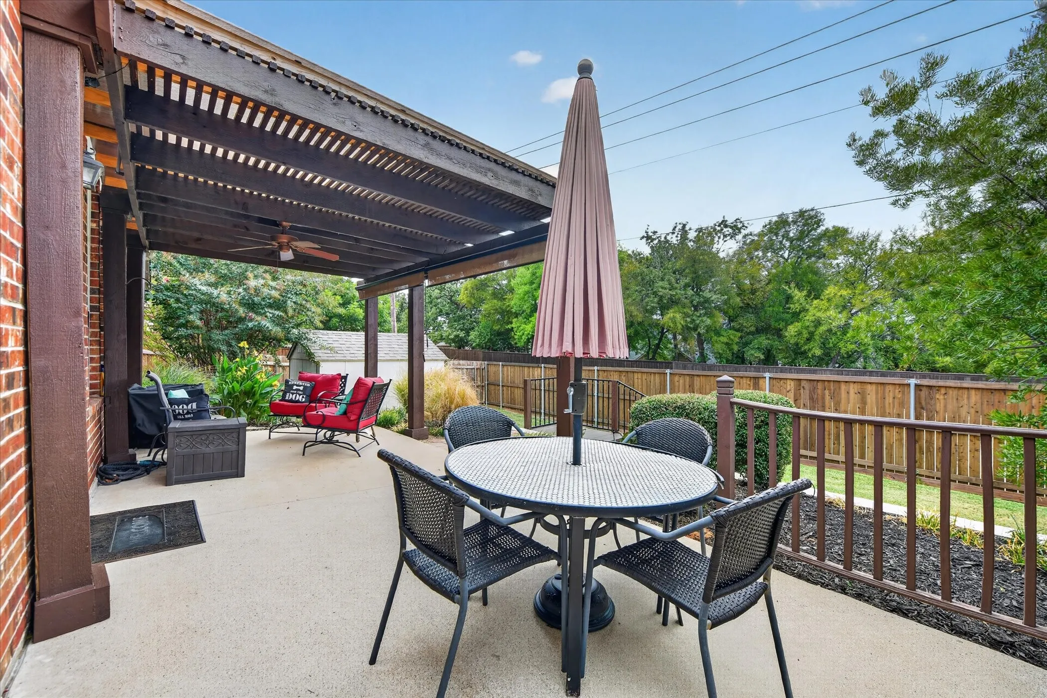 Expansive concrete patio featuring a wood pergola and ceiling fan, brick exterior accents, wood railing, and a wood privacy fence