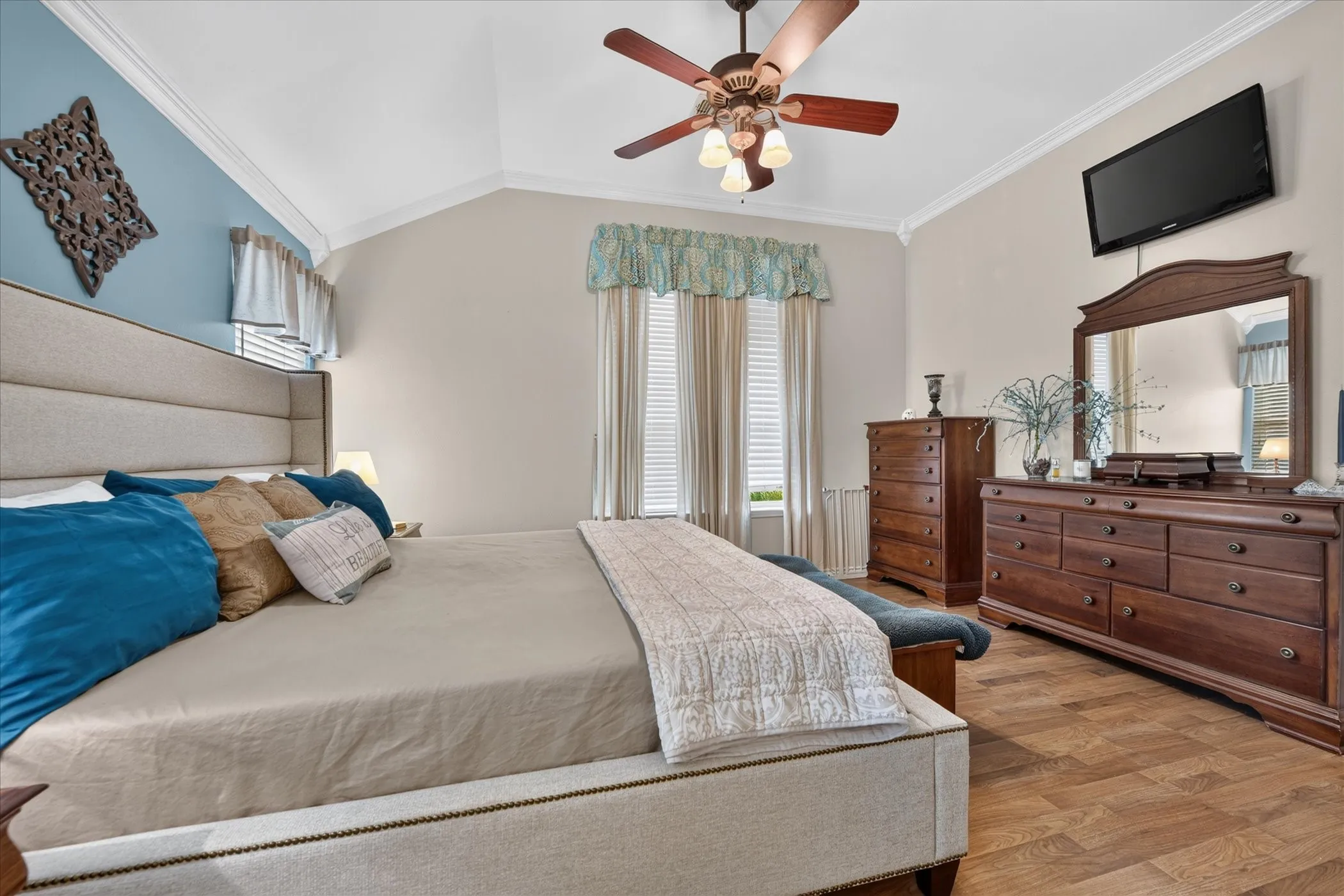 Vaulted ceiling with crown molding, ceiling fan with integrated lighting, wood-finish flooring, and multiple windows with blinds