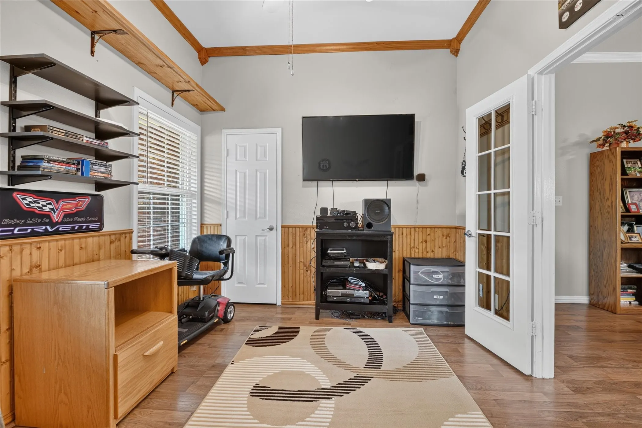 Vaulted ceiling with wood beams, wood-finish flooring, white paneled door, wood wainscoting, and a white French door
