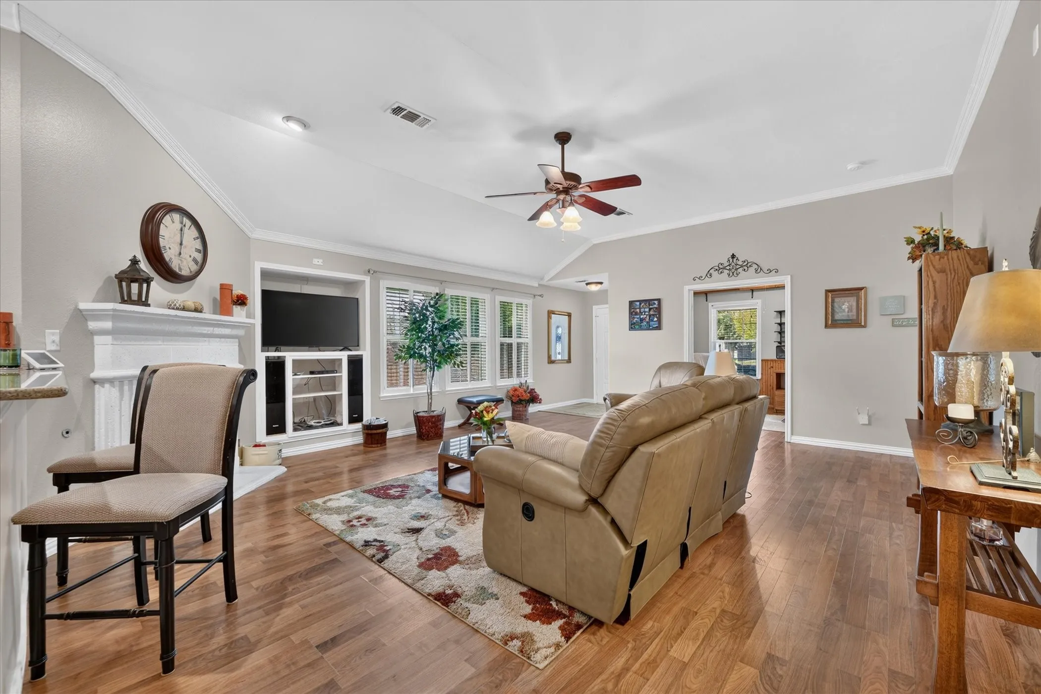Vaulted ceiling with a ceiling fan, recessed lighting, wood-finish flooring, built-in entertainment center, and a white mantel