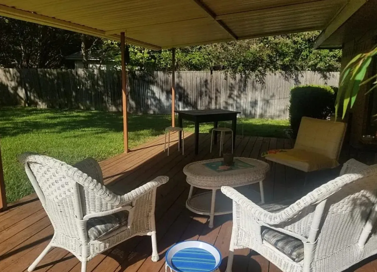 Expansive wooden deck with a covered patio structure, featuring a manicured lawn and a privacy fence
