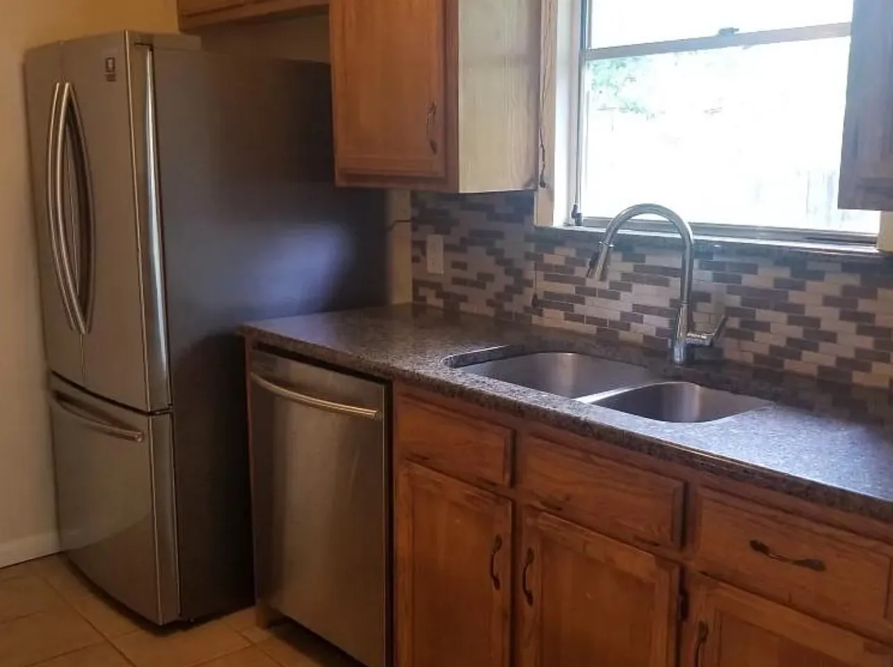 Stainless steel appliances, dual basin sink, wood cabinetry, stone-finish countertops, and mosaic tile backsplash