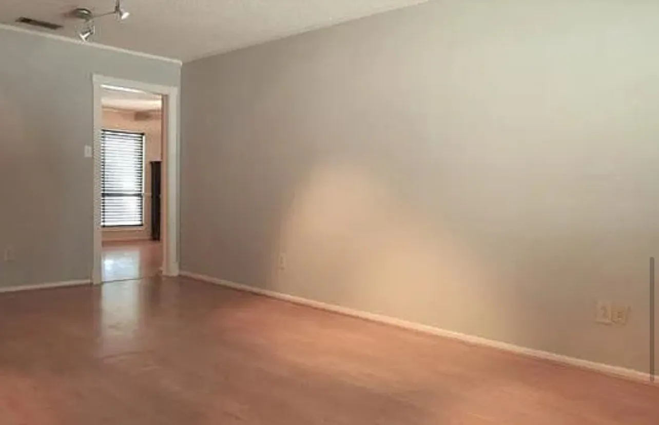 Wood-finish flooring with white baseboards, track lighting, and a doorway with white trim