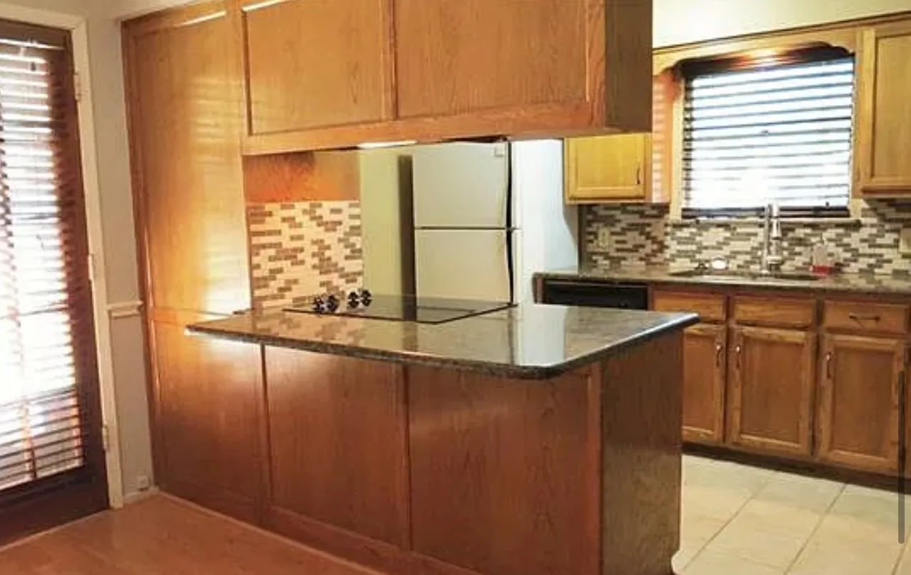 Kitchen featuring wood cabinetry, stone countertops, a tile backsplash, and an integrated cooktop