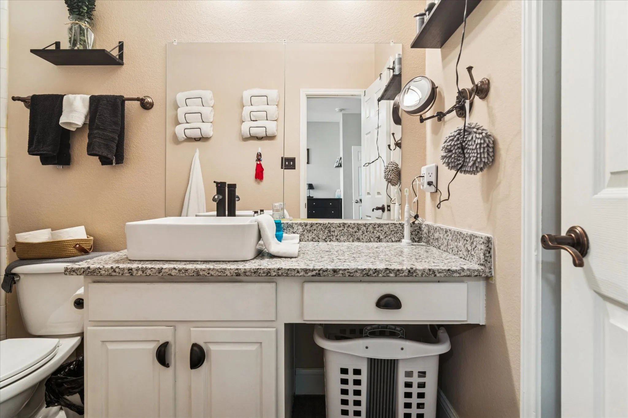 White vanity cabinetry with matte black hardware, a rectangular vessel sink, a black wall-mounted faucet, and a large vanity mirror