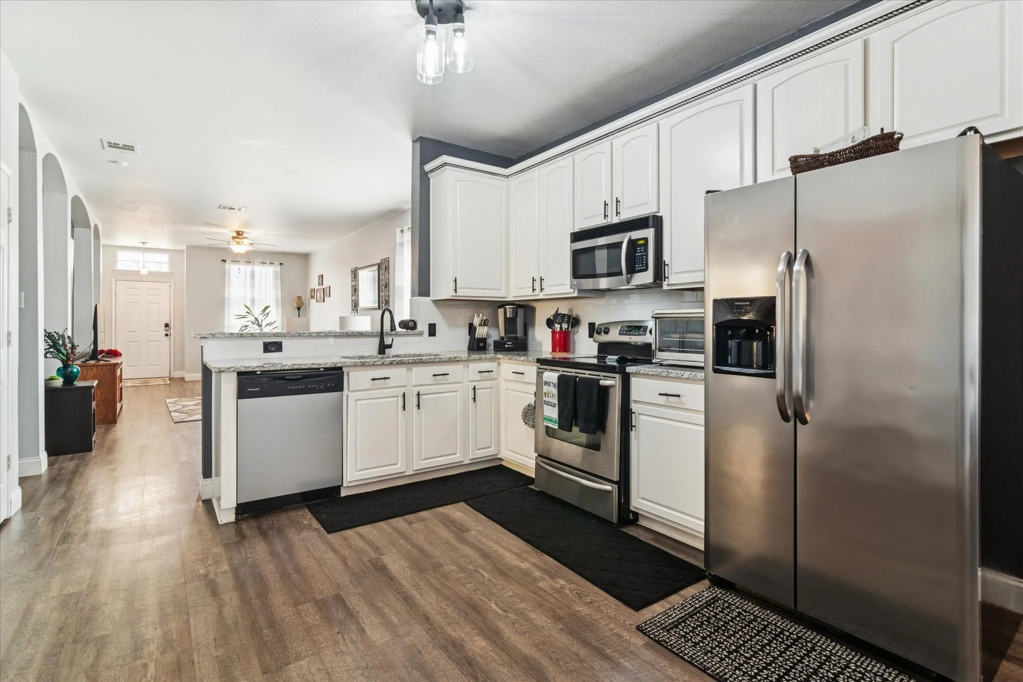 Kitchen featuring white cabinetry, stainless steel appliances, wood-finish flooring, and a breakfast bar