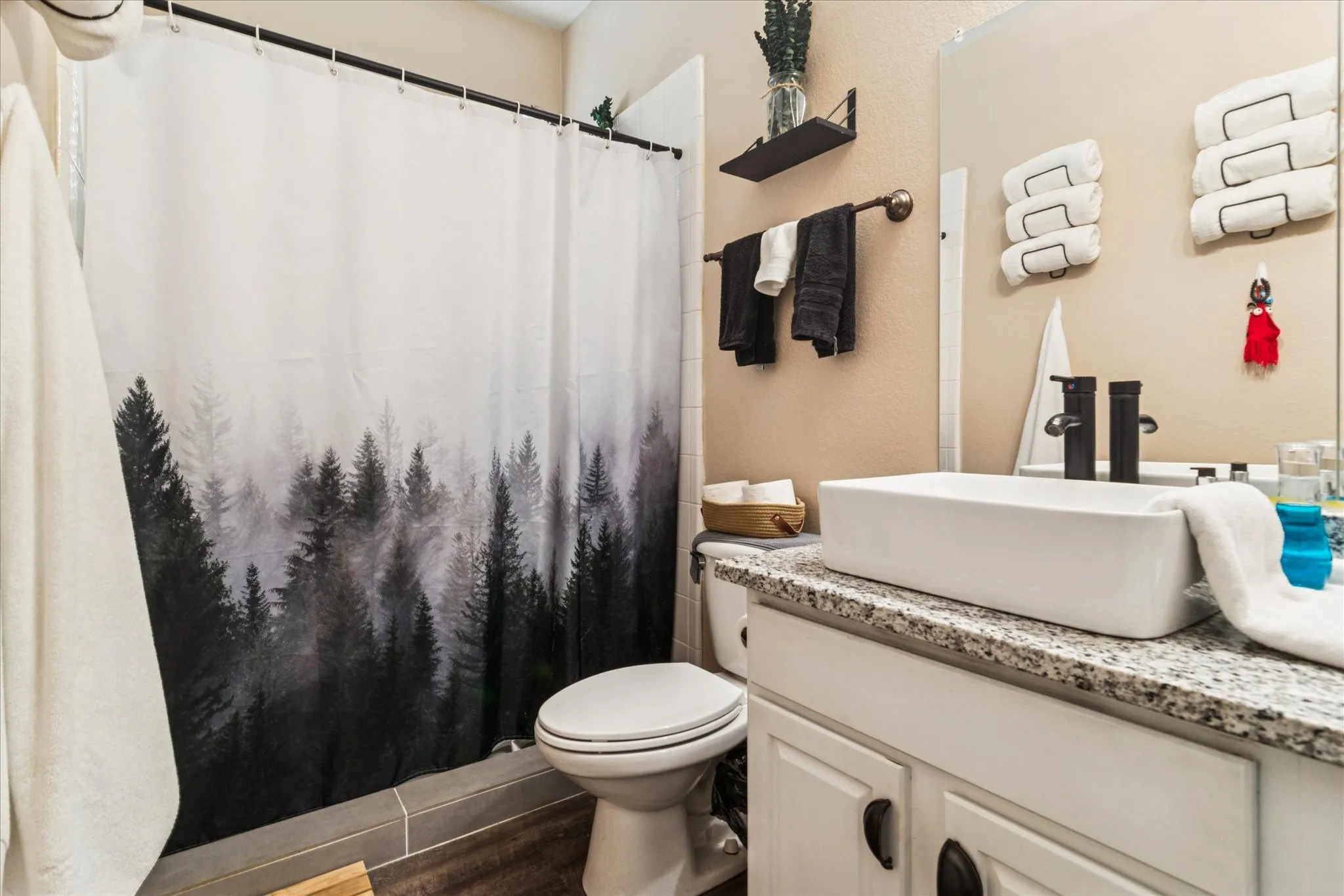 Bathroom featuring a vessel sink, dual matte black faucets, granite-style countertop, white vanity cabinetry, and a built-in shower/tub combination
