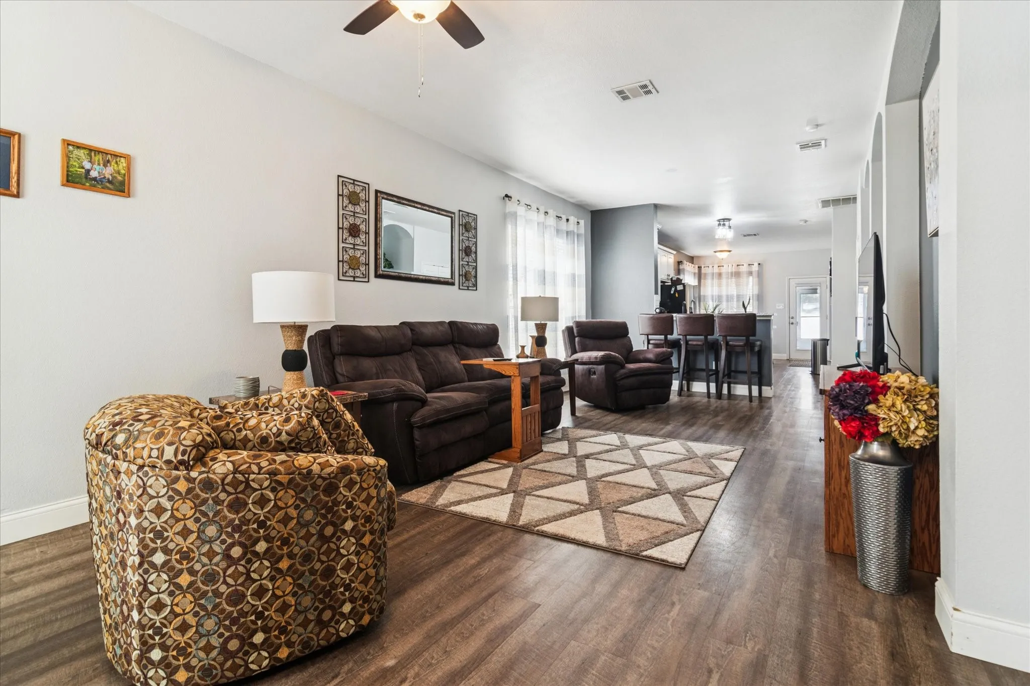 Wood-finish flooring throughout, light-toned wall paint, ceiling fan with integrated lighting, recessed lighting, and a partial view of a kitchen bar area