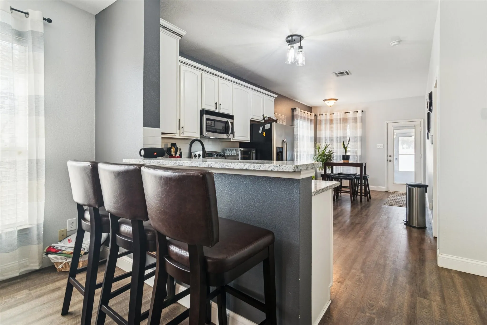 White shaker cabinetry, black appliances, light-toned countertops, and wood-finish flooring