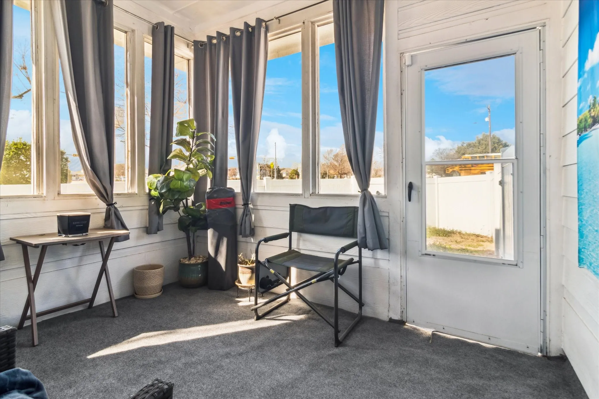 Enclosed porch with multiple picture windows, white painted wood panel walls, a white entry door with glass pane, and gray carpeting