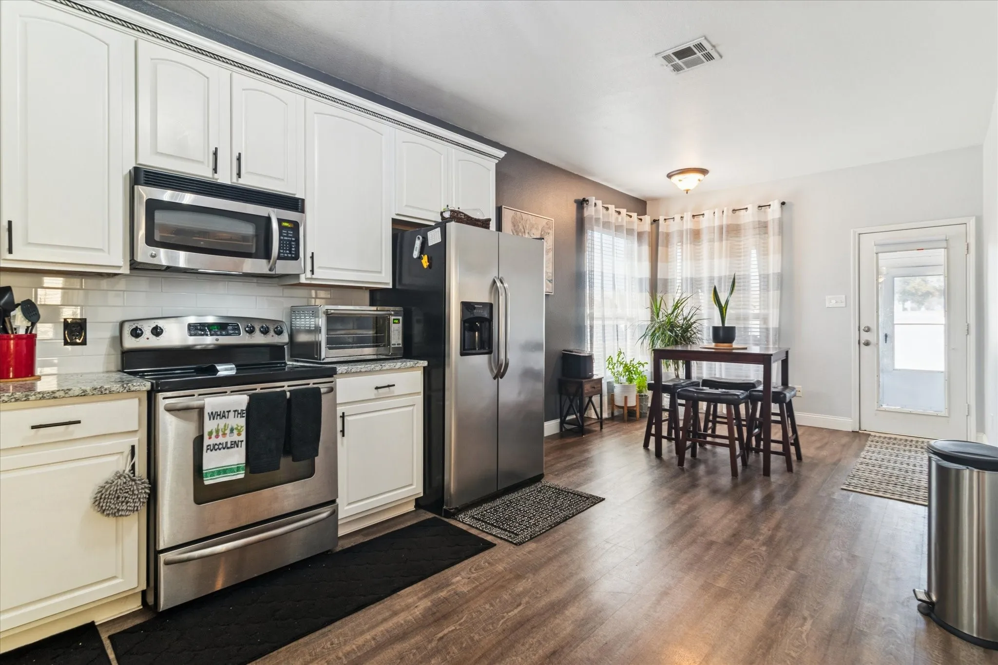 Kitchen featuring white cabinetry, stainless steel appliances, speckled countertops, and wood-finish flooring
