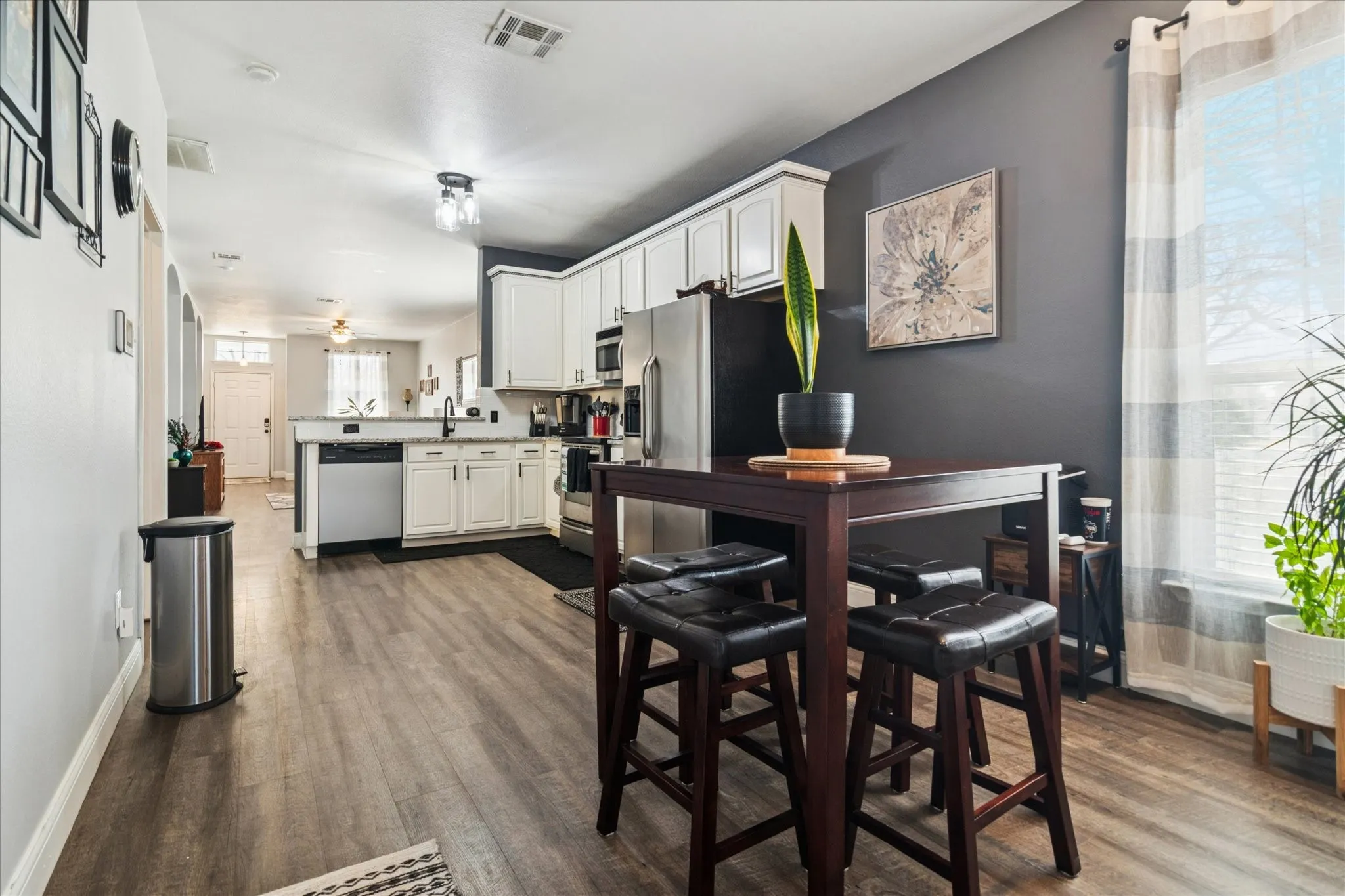 Kitchen featuring white cabinetry, stainless steel appliances, wood-finish flooring, and a window with blinds