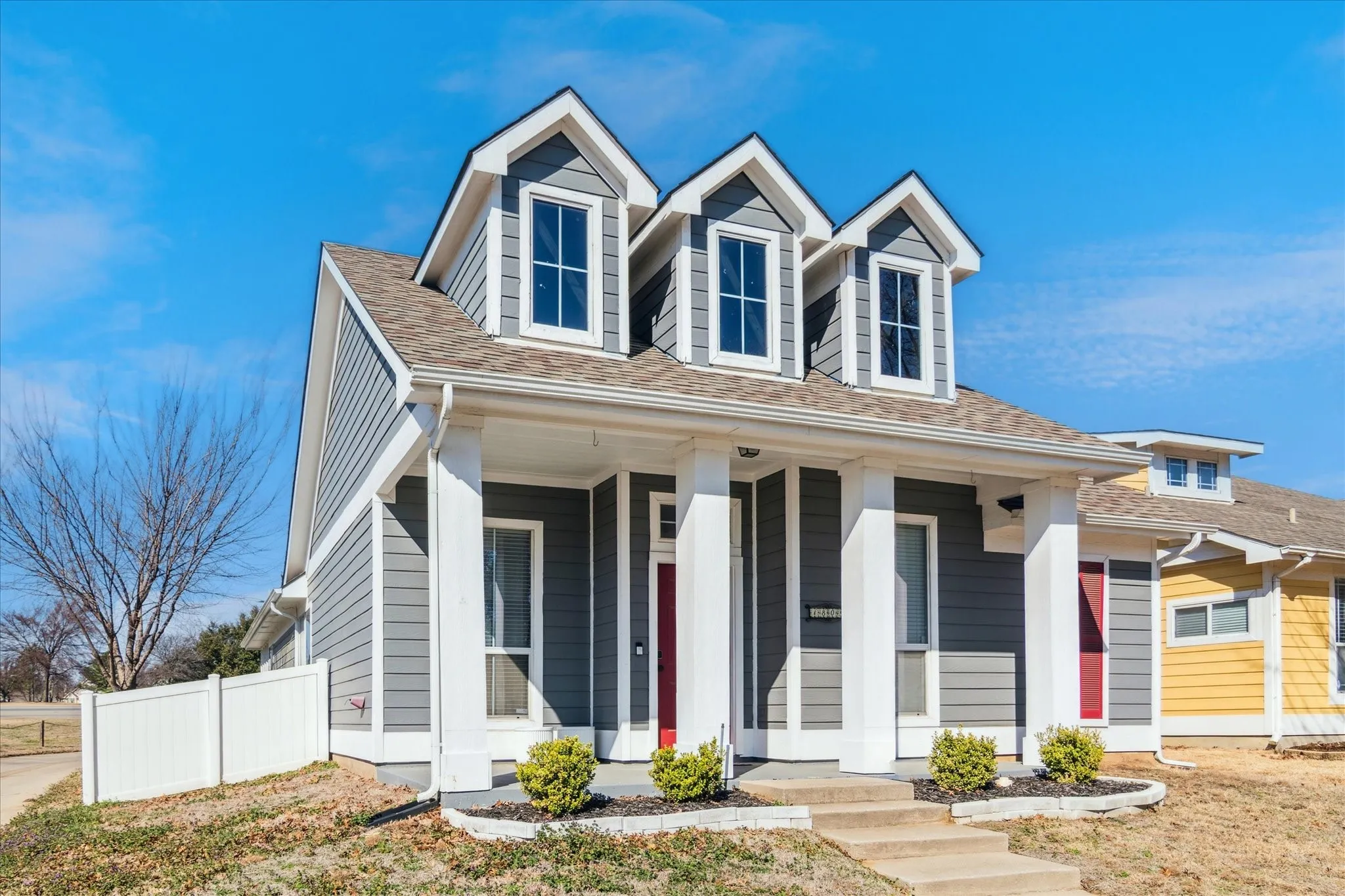 Gray siding exterior with white trim, three dormer windows, a covered entry porch, and a red front door
