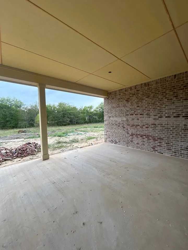 Spacious covered patio with concrete flooring, brick exterior wall, and substantial support columns