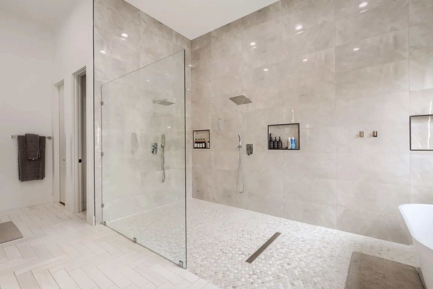 Walk-in shower with full-height glass enclosure, rain showerhead, recessed wall niches, and pebble-tile flooring
