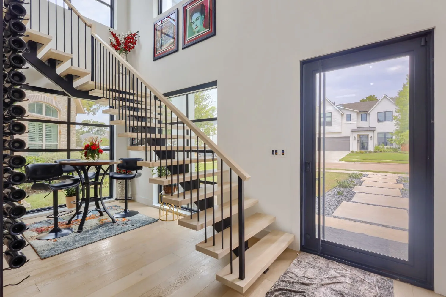 Open-concept entry with wood-finish flooring, a floating staircase, and a floor-to-ceiling glass panel door