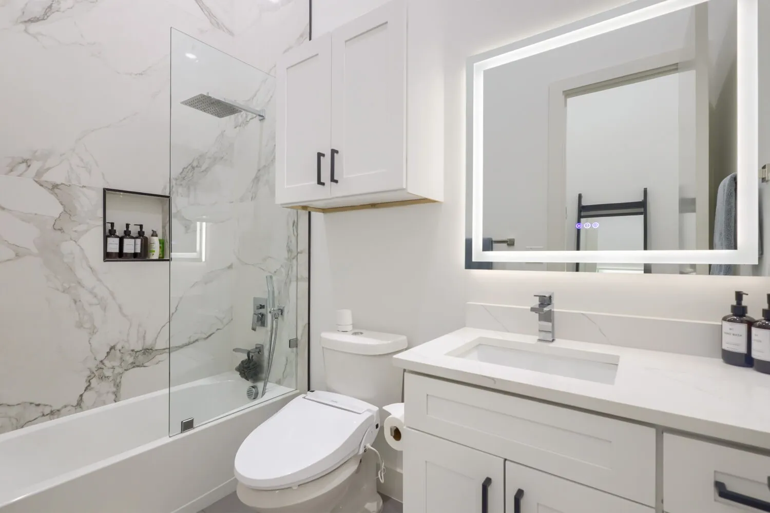 White vanity with quartz countertop, undermount sink, and illuminated mirror