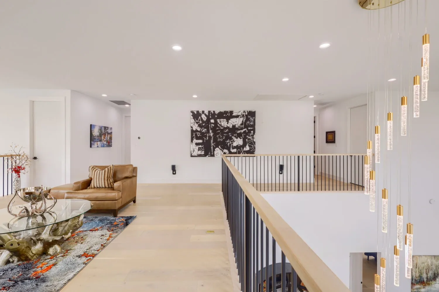 Open concept upper level featuring light wood-finish flooring, recessed lighting, a modern railing with vertical balusters, and a contemporary chandelier with multiple hanging pendants
