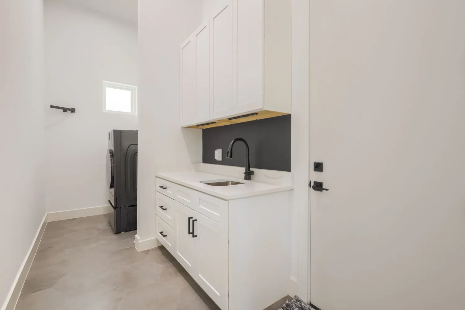 Laundry area featuring white cabinetry, a sink with a matte black gooseneck faucet, light-toned countertop, and hexagonal floor tiling