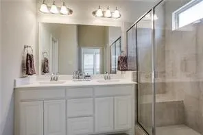 Dual vanity with integrated sinks, white cabinetry, large vanity mirror, glass-enclosed shower, and a built-in shower bench