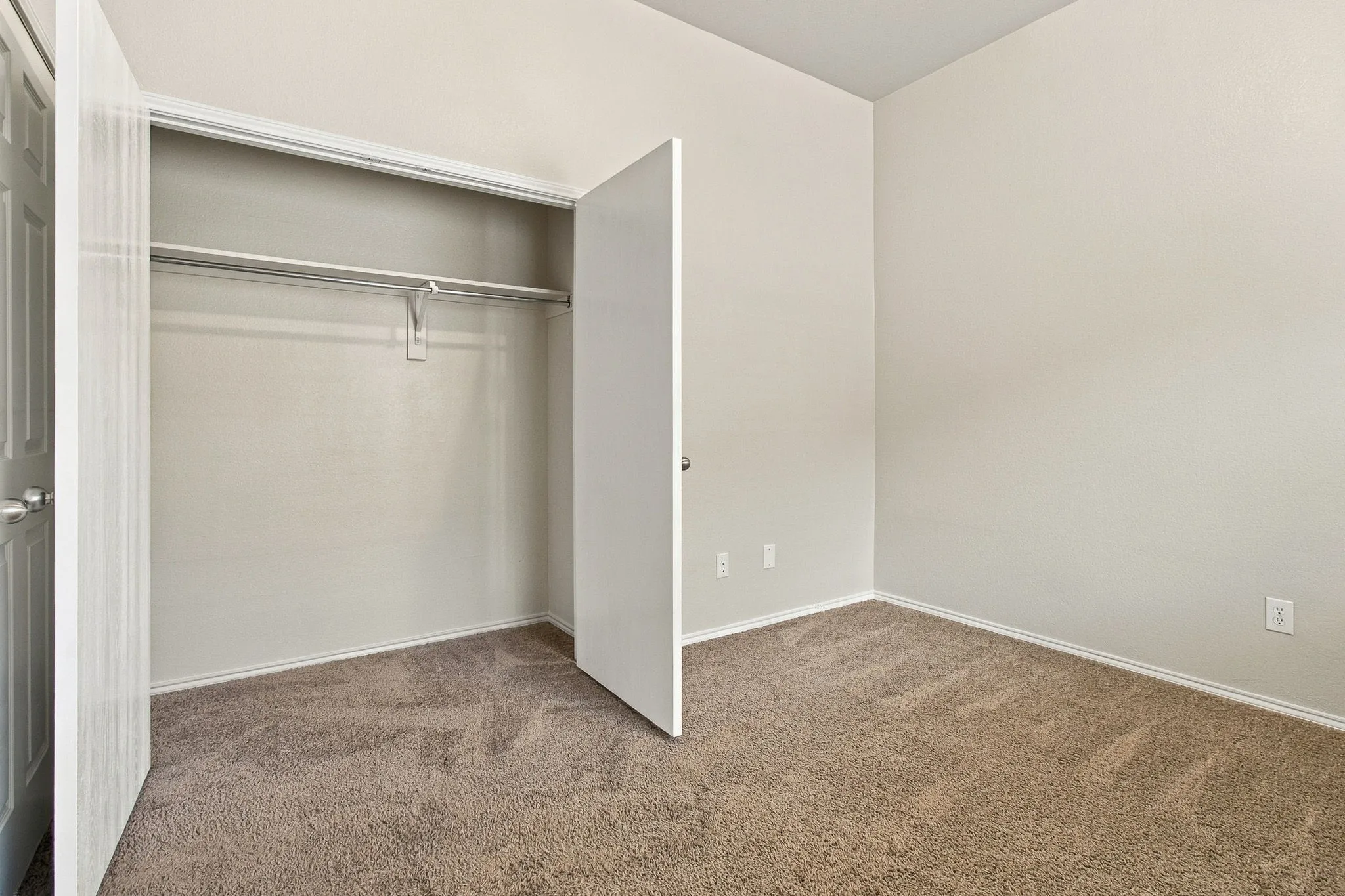 Wall-to-wall carpeting, neutral wall finishes, closet with shelving and hanging rod, and white trim