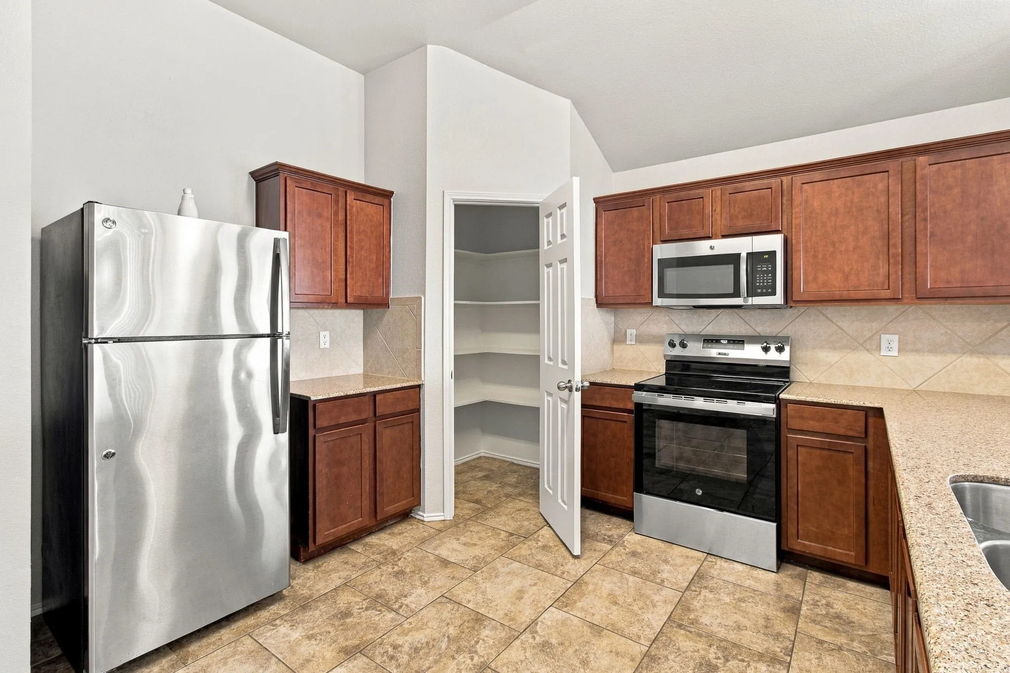 Stainless steel appliances, built-in microwave, ample cabinetry, tiled flooring, and a walk-in pantry