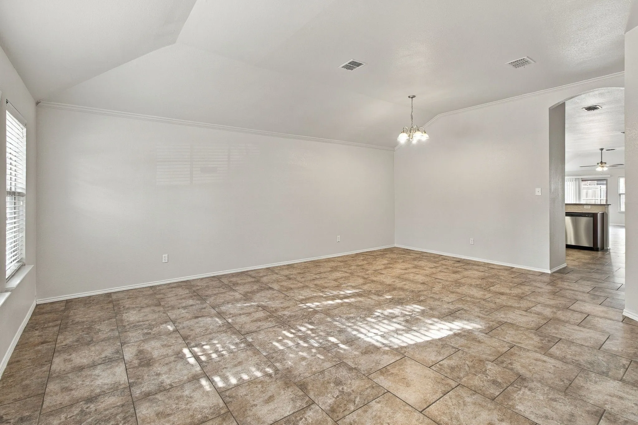 Vaulted ceiling, crown molding, tiled flooring, arched doorway, and a brass chandelier