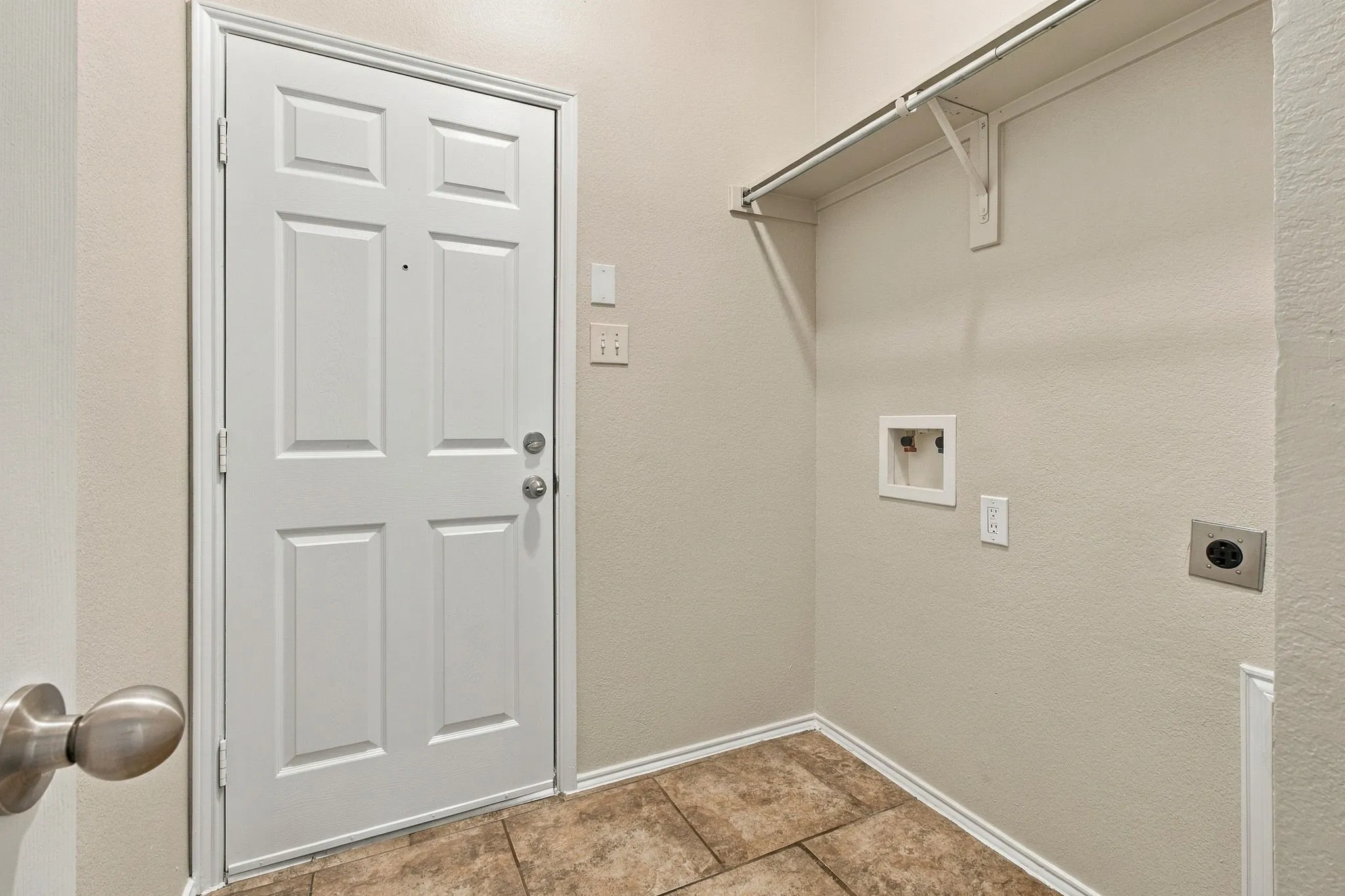 Utility area with tile flooring, a white interior door, and a built-in shelf with a clothing rod