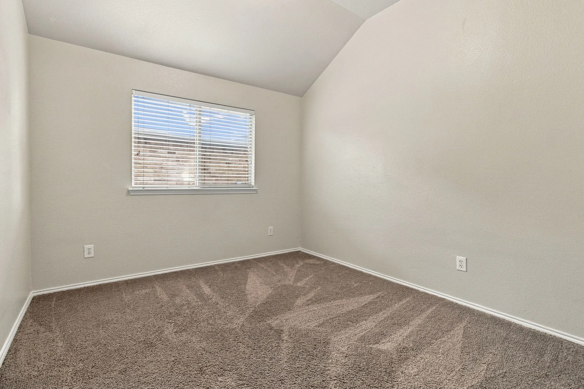 Sloped ceiling room featuring a window with horizontal blinds and neutral-toned textured carpet
