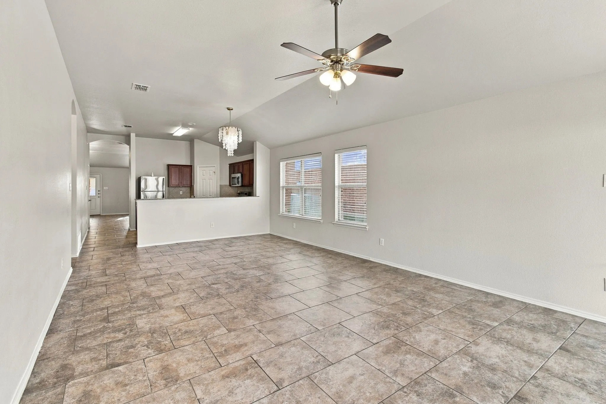Vaulted ceiling with a ceiling fan, dual windows, tile flooring, and a kitchen featuring dark wood cabinetry and stainless steel appliances