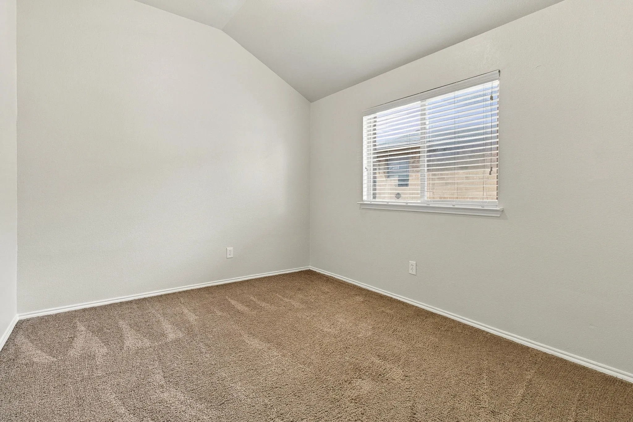 Vaulted ceiling with an angled wall, neutral carpet, and a window with blinds