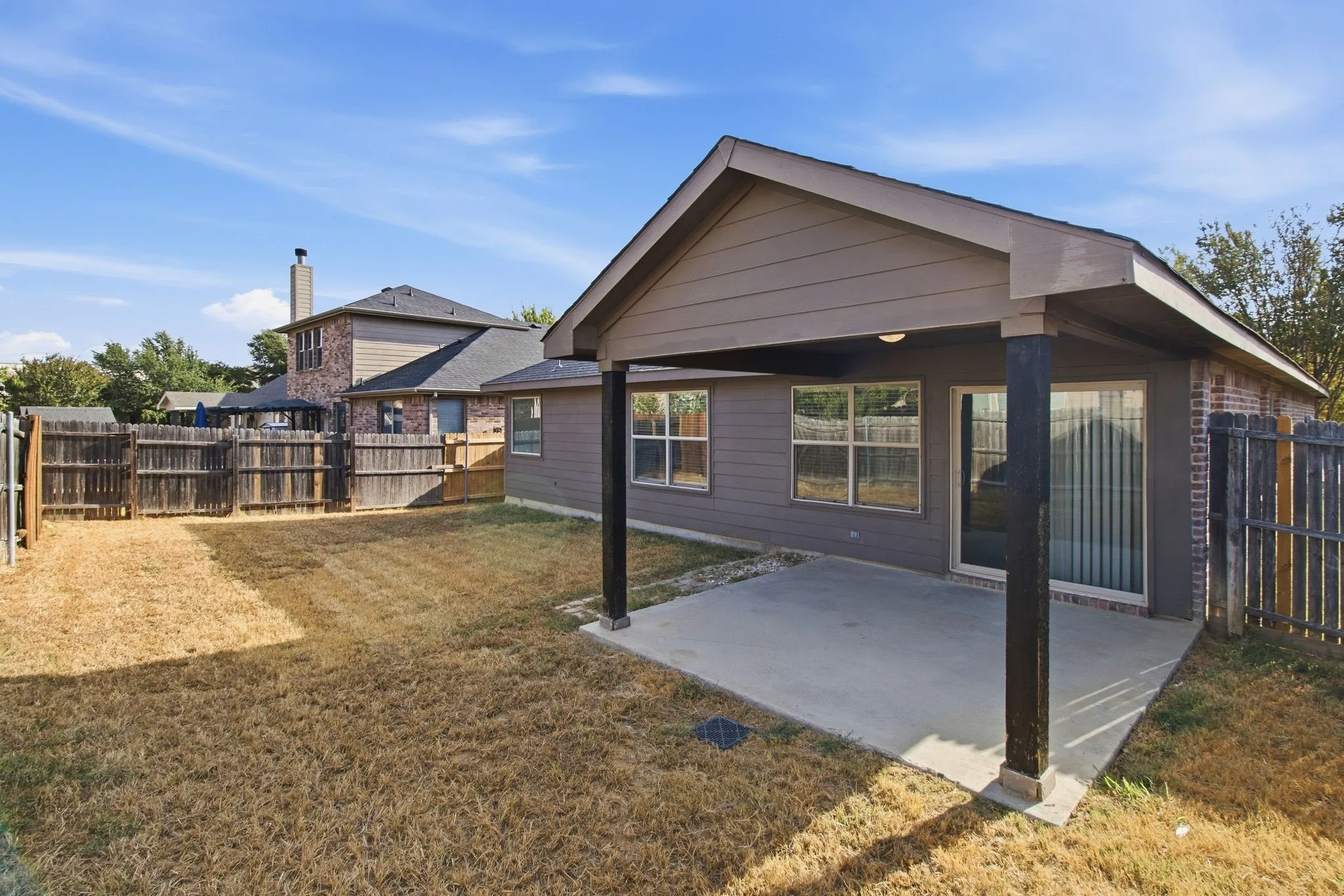Covered patio with concrete flooring, framed by a wood privacy fence