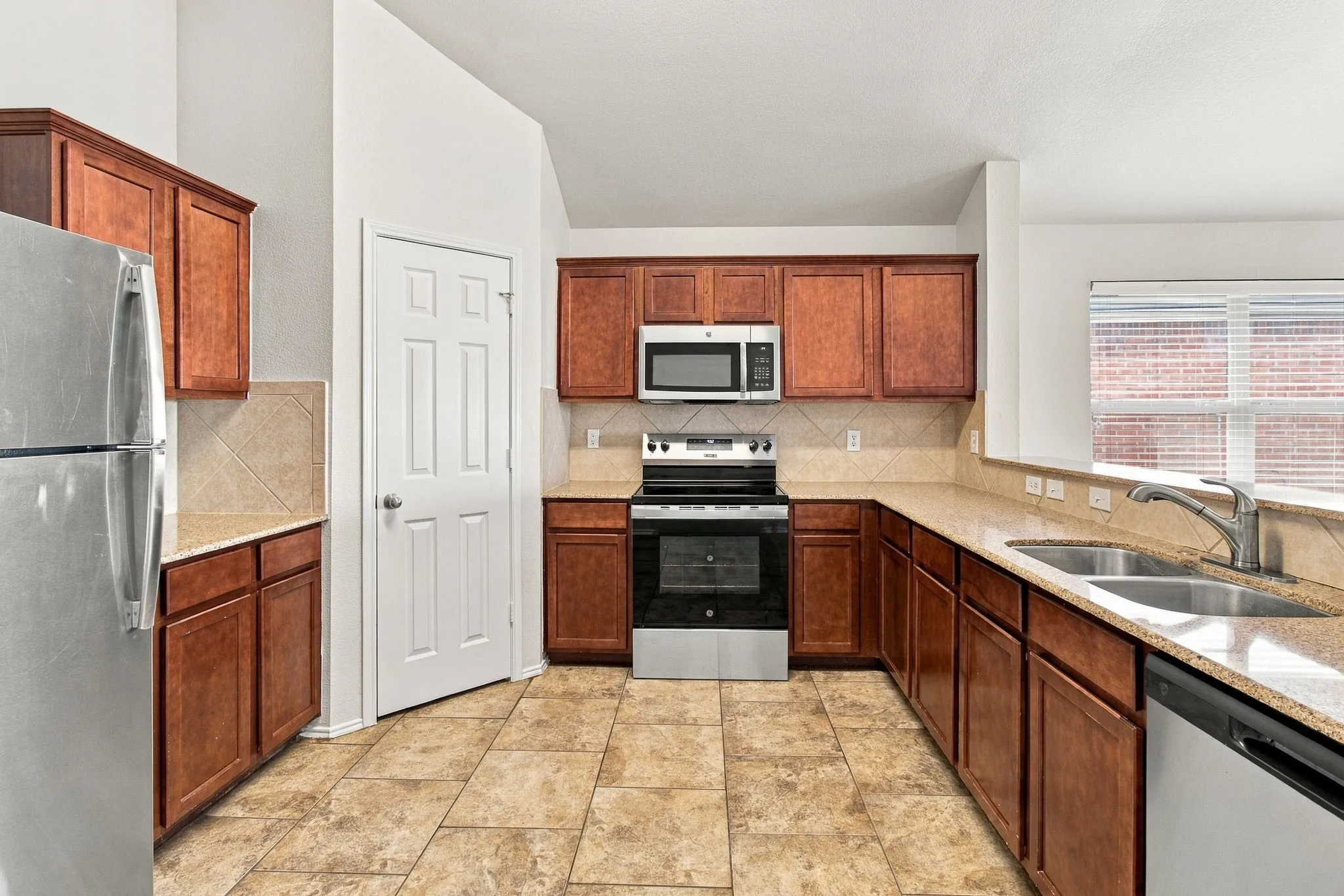 Kitchen featuring wood-finish cabinetry, tile flooring, stone-finish countertops, stainless steel appliances, and a double basin sink with a chrome faucet