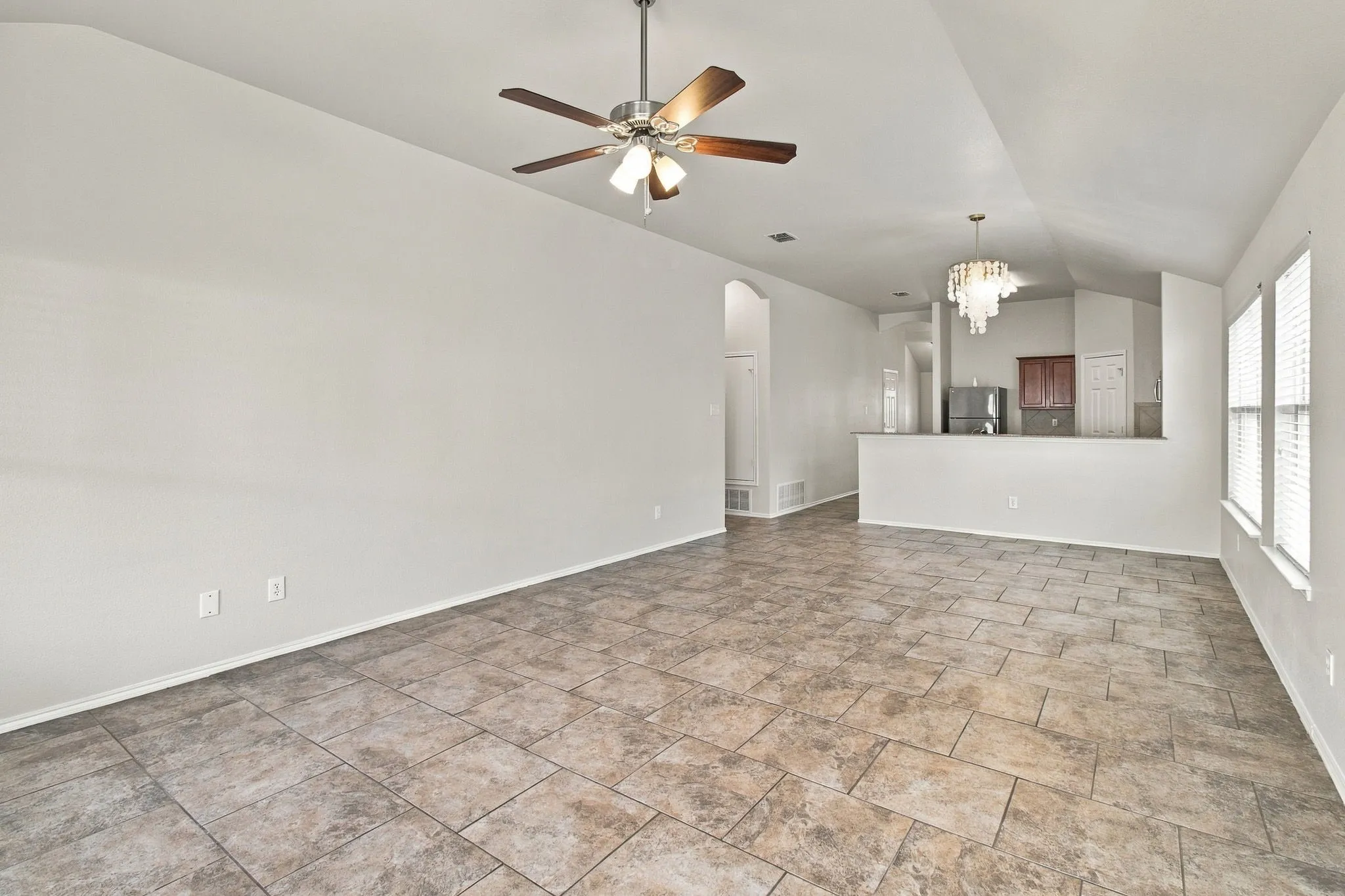 Vaulted ceilings with a ceiling fan, tiled flooring, arched doorway, and a decorative chandelier