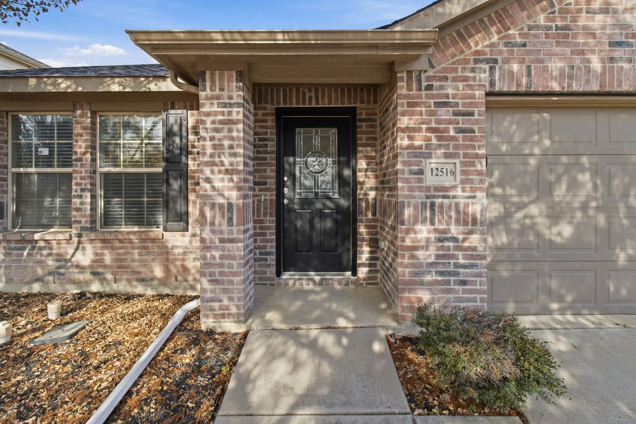Brick facade with a covered entry, dark paneled front door with decorative glass, and attached garage