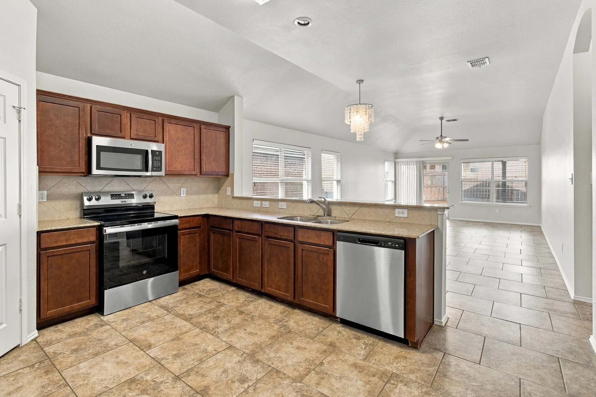 Kitchen featuring rich wood cabinetry, stainless steel appliances, tile flooring, and a stone-look countertop with an undermount sink