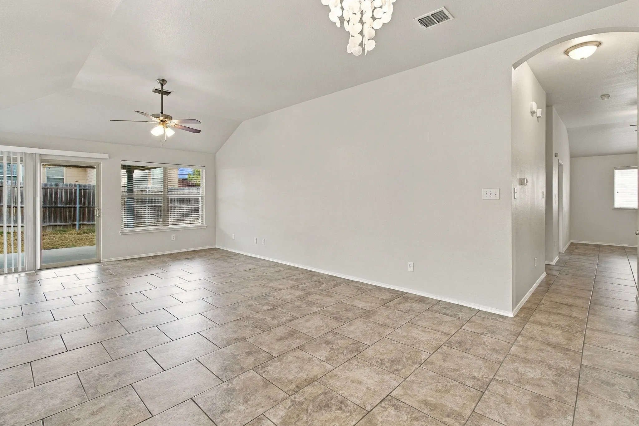 Vaulted ceiling, ceiling fan, tile flooring, sliding glass door, and arched doorway