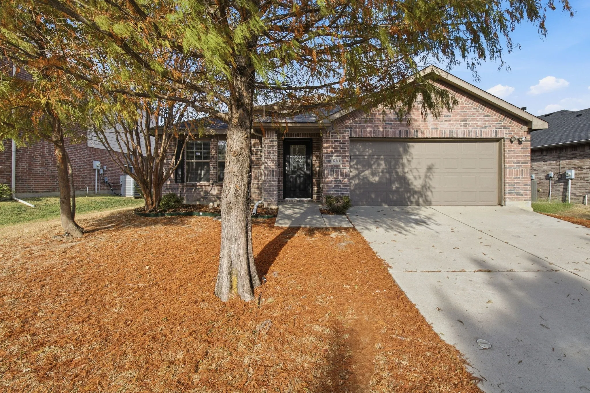 Brick exterior with an attached garage, concrete driveway, and mature landscaping